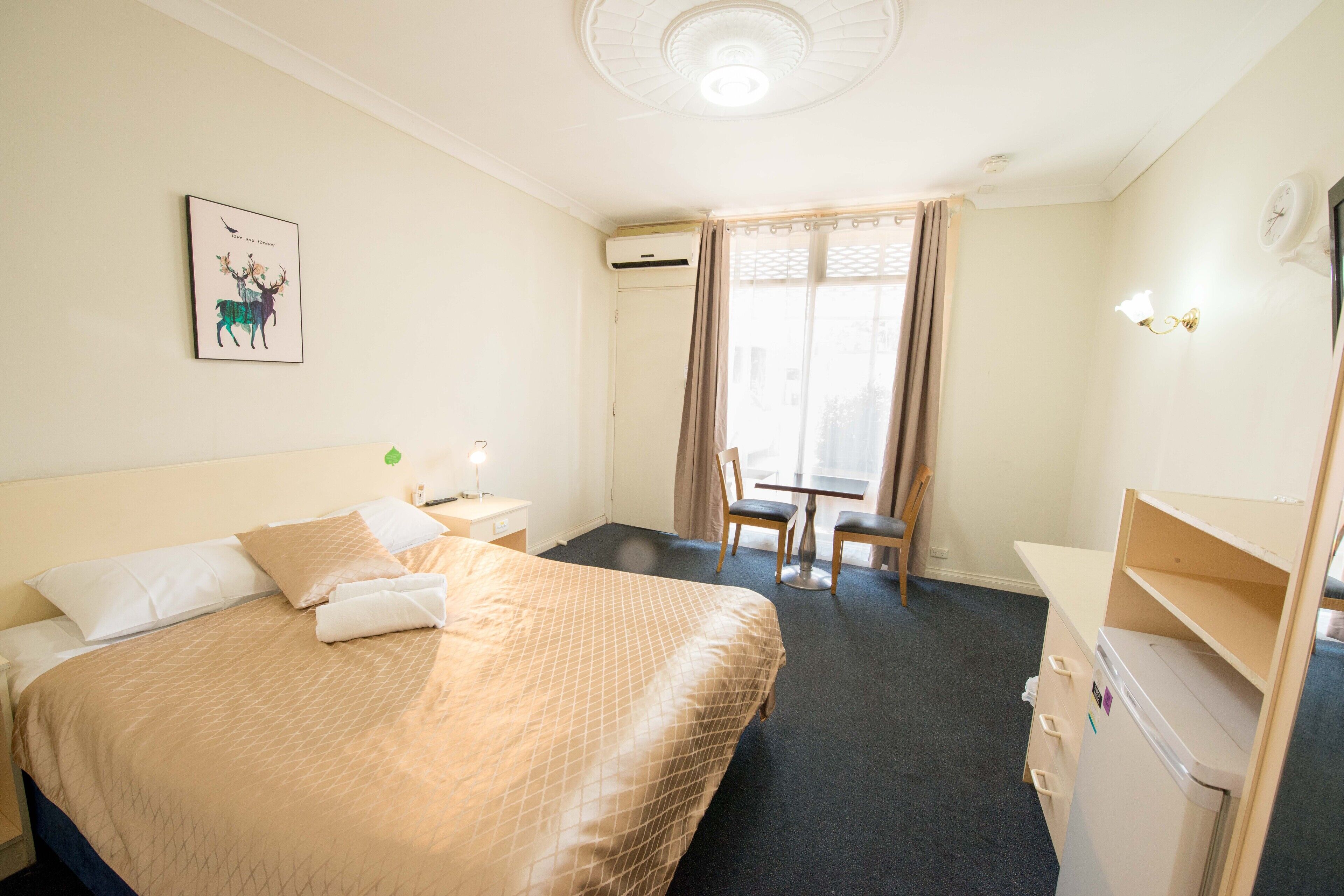 Habitación de hotel con cama, escritorio, silla, mesita y equipo de aire acondicionado.