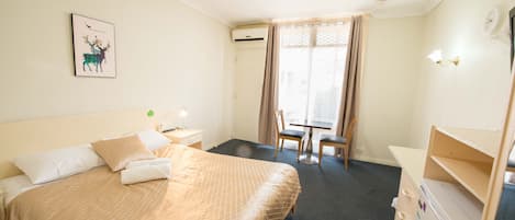Habitación de hotel con cama, escritorio, silla, mesita y equipo de aire acondicionado.
