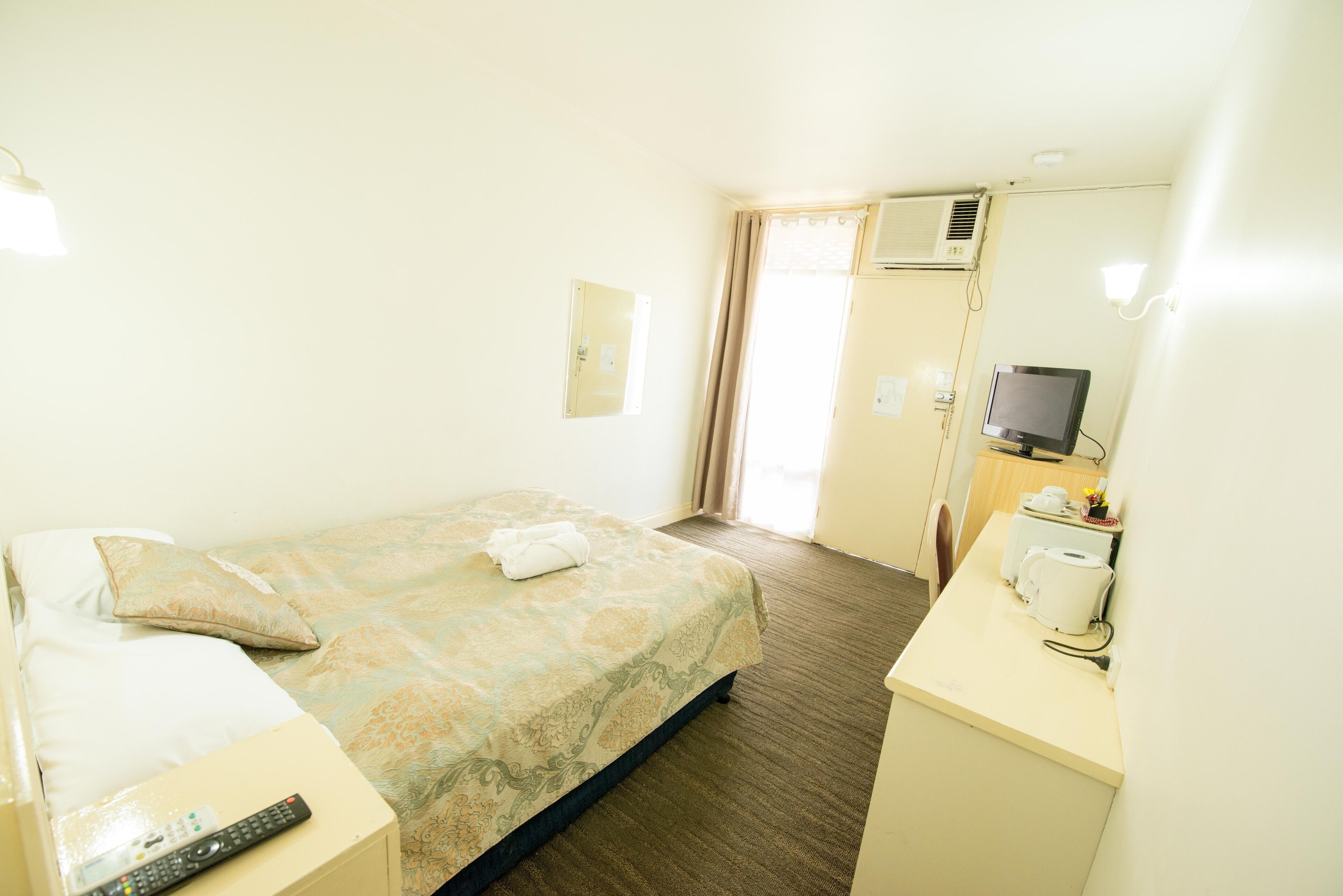 Una habitación de hotel con cama, escritorio, teléfono y una taza, televisión y aire acondicionado.