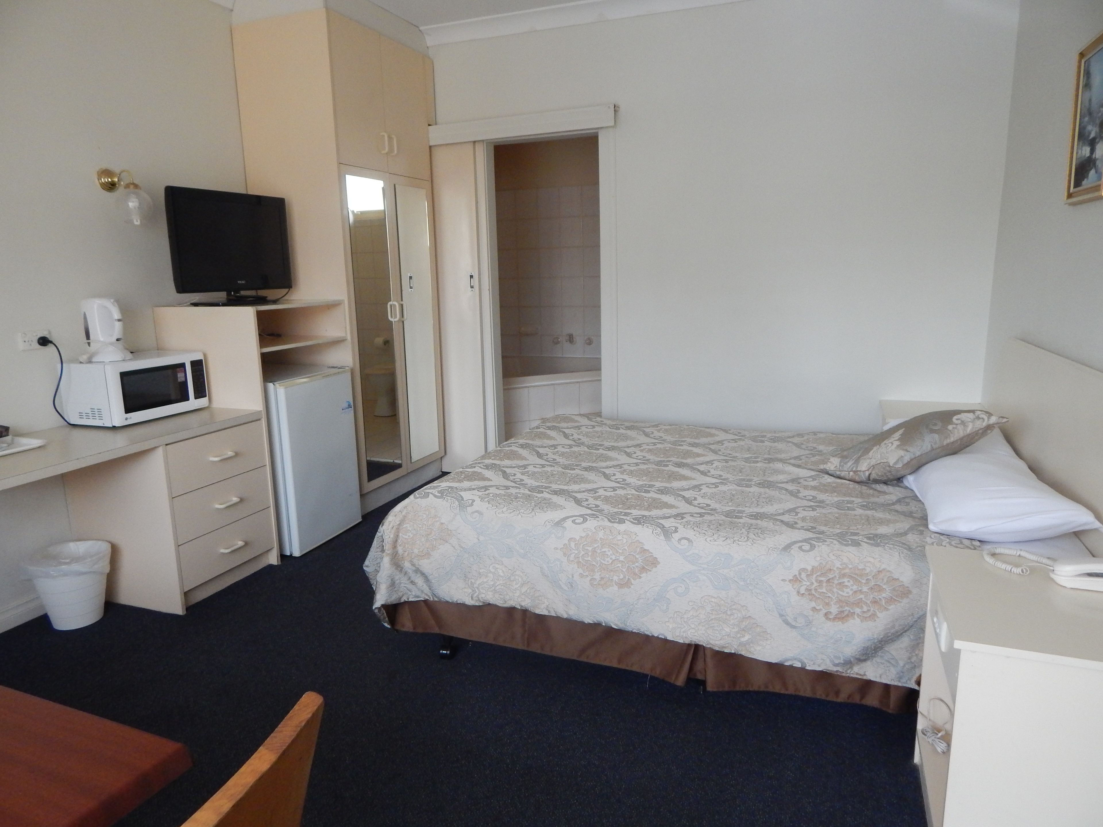 A hotel room with a bed, a desk with a computer, a microwave, and a small refrigerator.