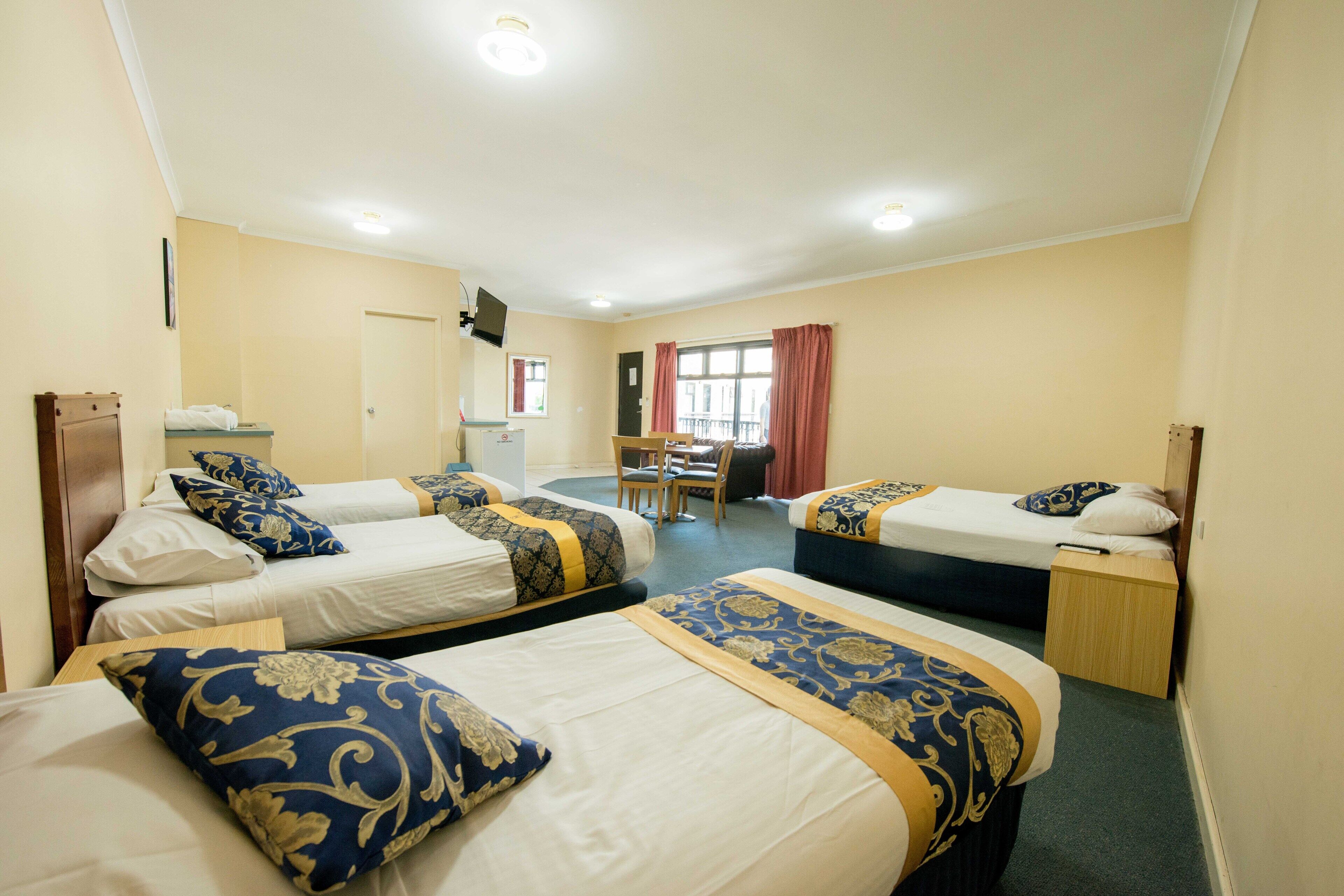 A hotel room with three single beds, a desk, a chair, and a window with curtains.