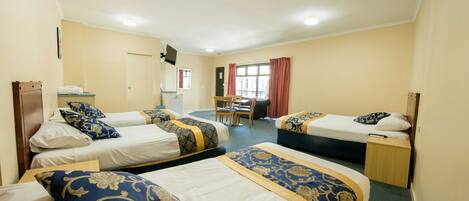A hotel room with three single beds, a desk, a chair, and a window with curtains.