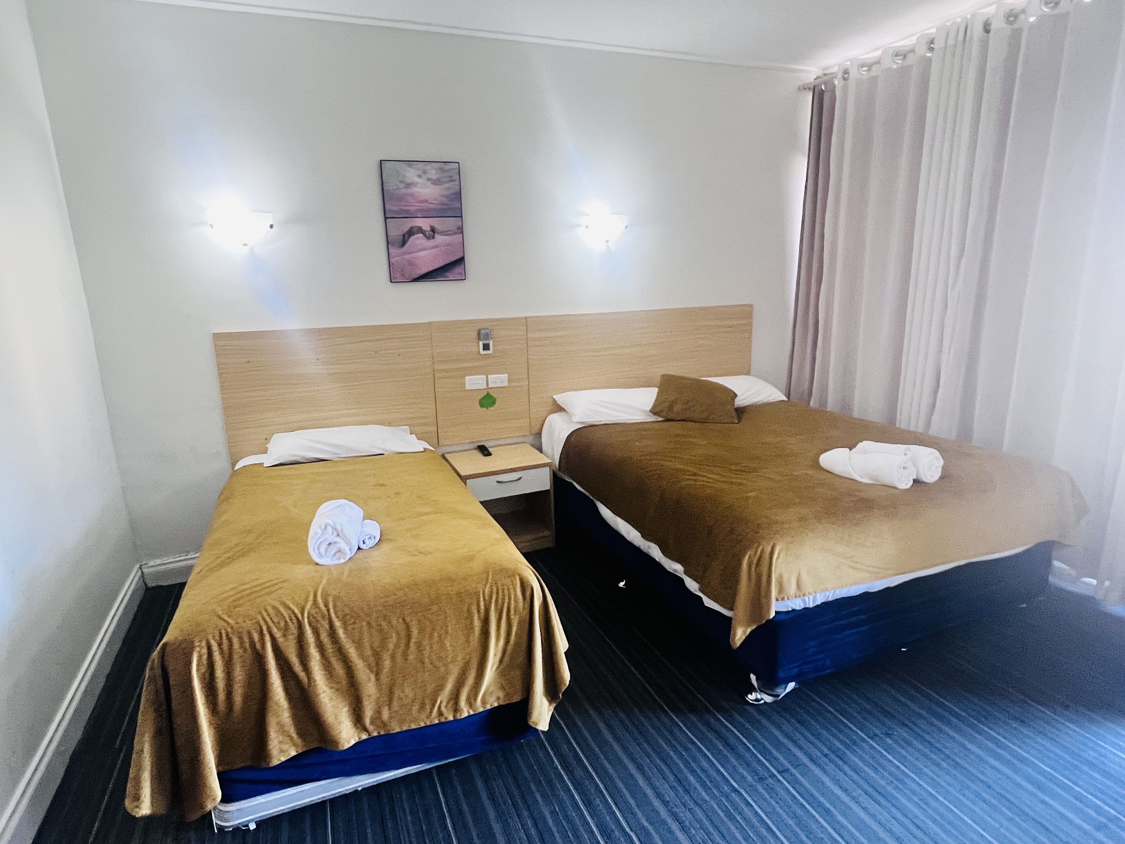 A hotel room with two beds, a nightstand, a wall-mounted phone, and a painting.