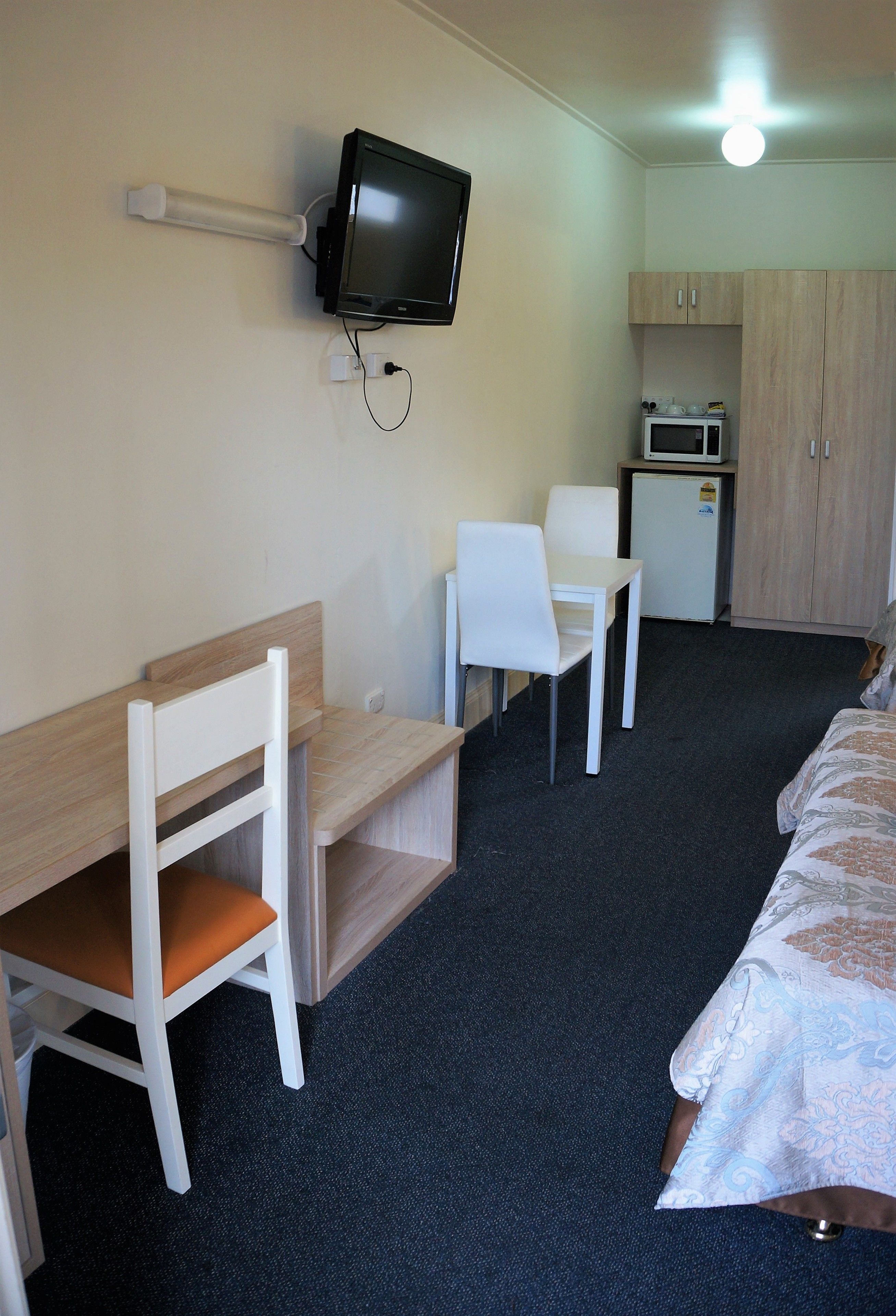 A room with a bed, a desk with a chair, a television, a microwave, and a small kitchenette.