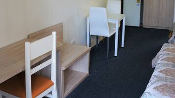A room with a bed, a desk with a chair, a television, a microwave, and a small kitchenette.