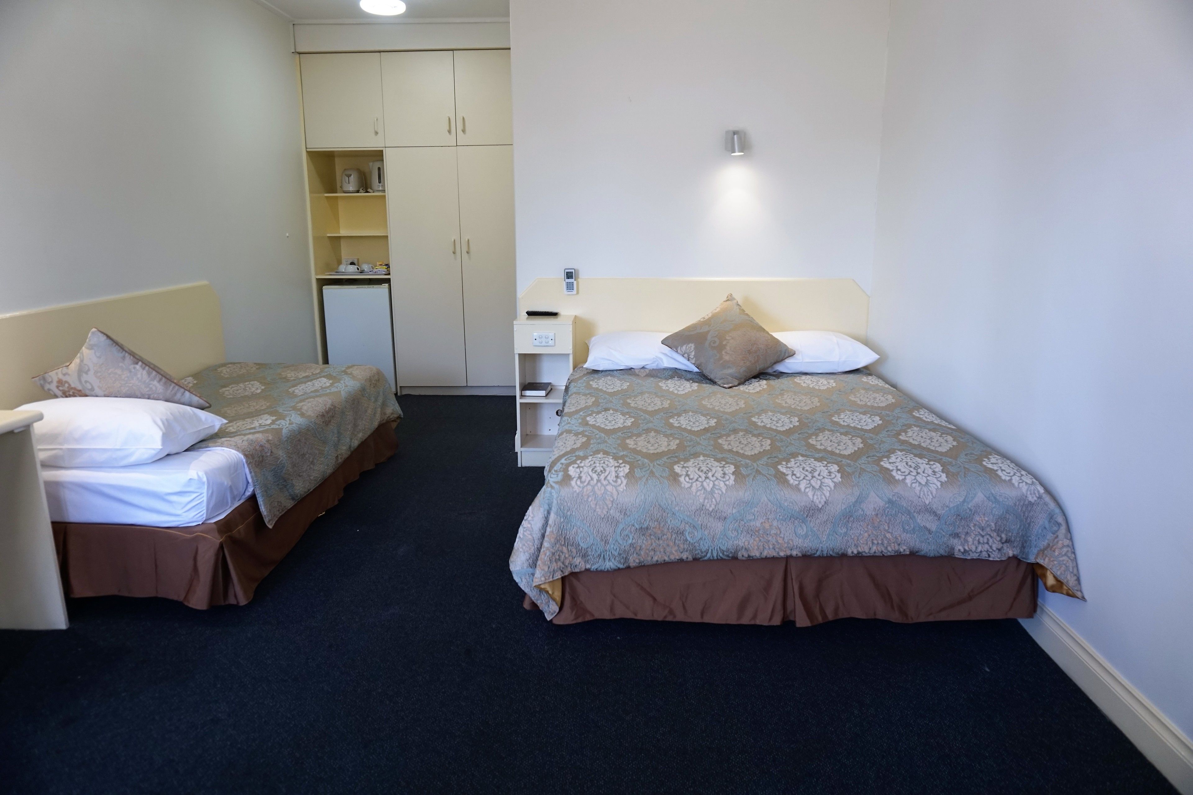 A hotel room with two single beds, a small desk, a wardrobe, and a nightstand.