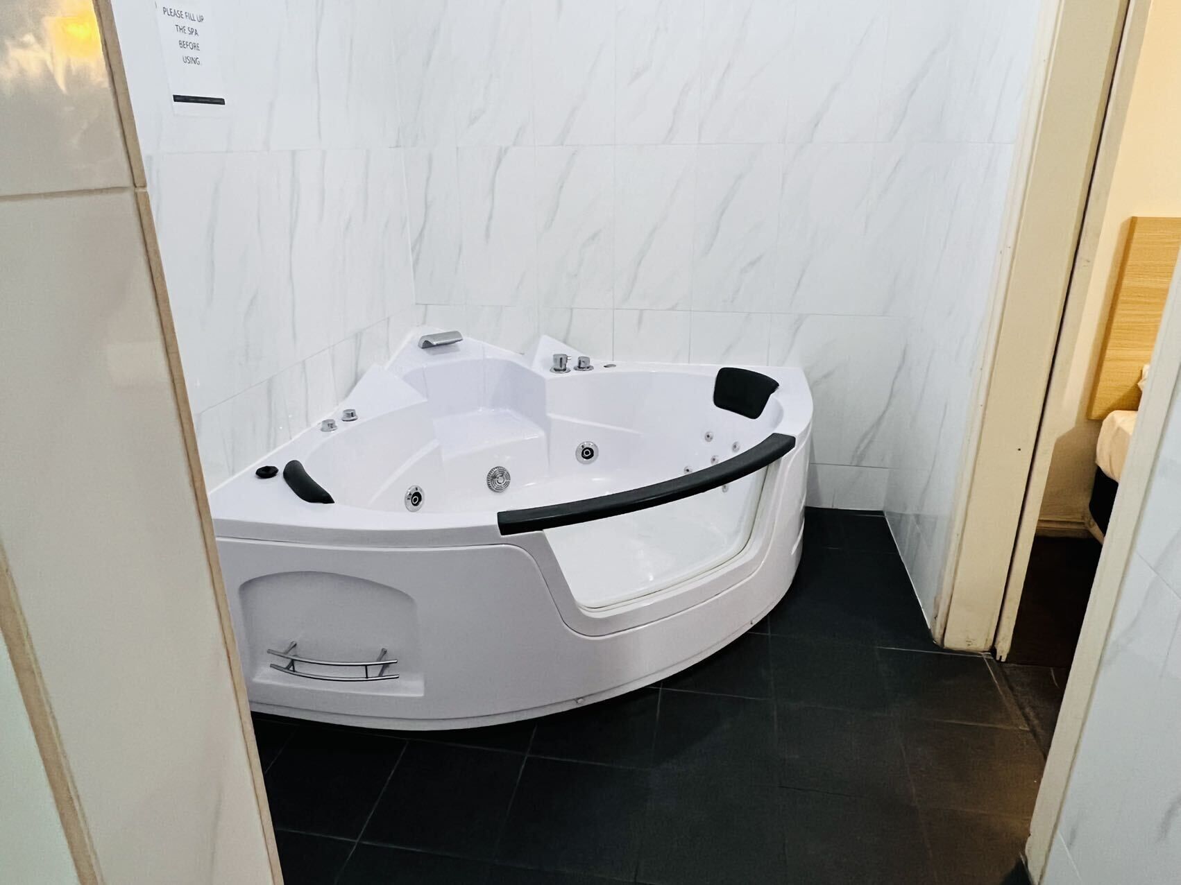Un baño tipo spa con una bañera blanca, baldosas de piso negras y una pared de mármol blanco.