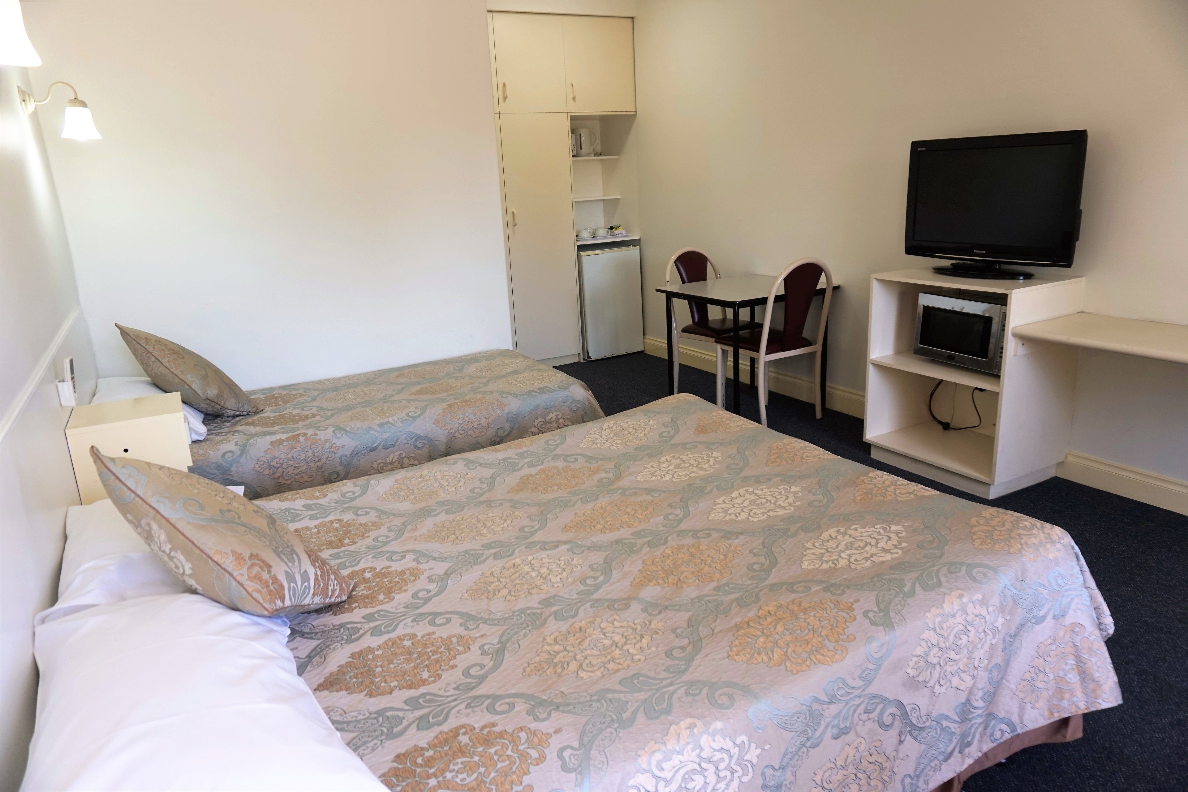 Una habitación de hotel con dos camas, un escritorio, una silla, un televisor y un refrigerador pequeño.