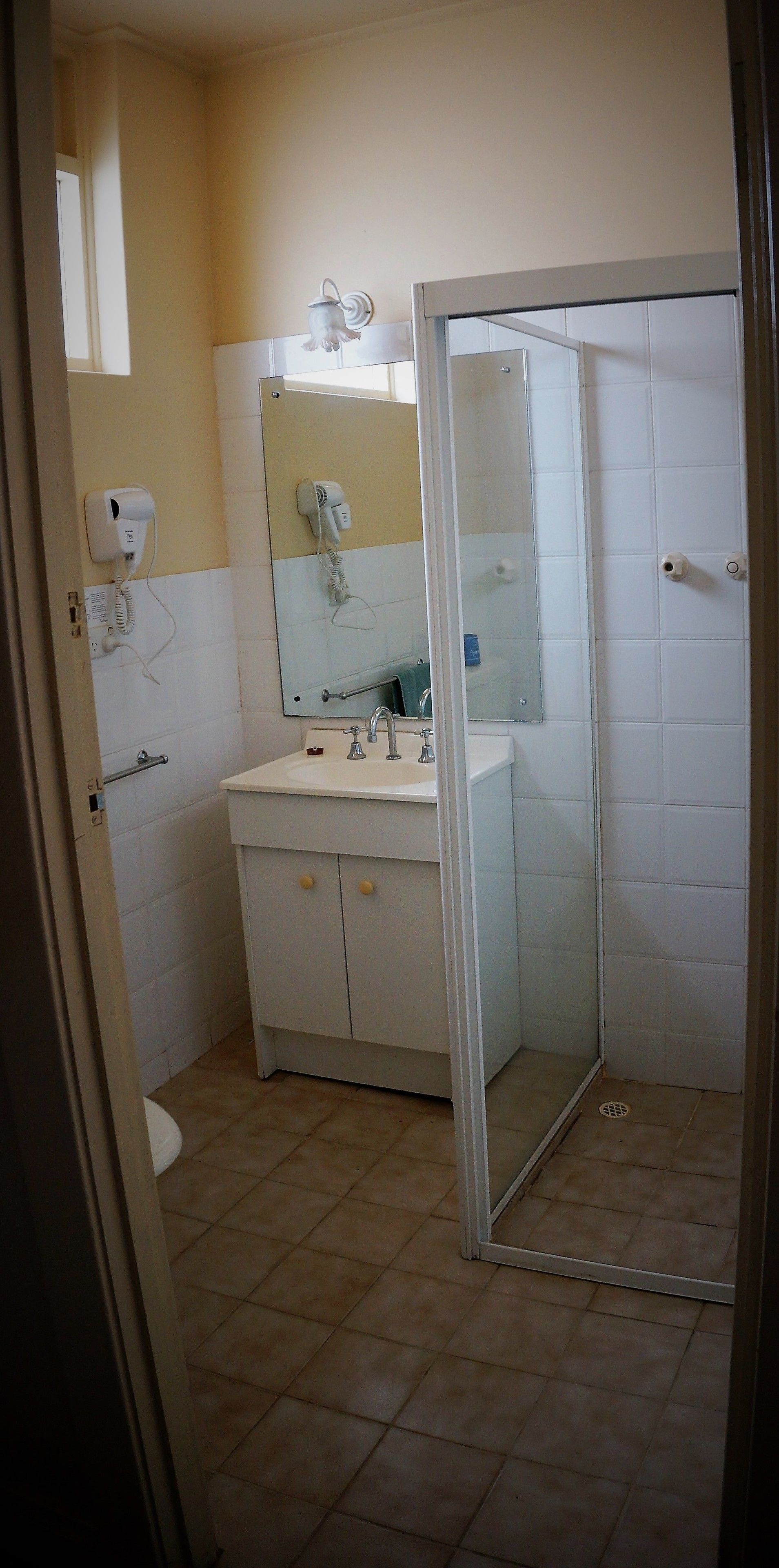 Un baño con lavamanos blanco, espejo, secador de pelo y cabina de ducha de vidrio.