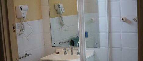 Un baño con lavamanos blanco, espejo, secador de pelo y cabina de ducha de vidrio.