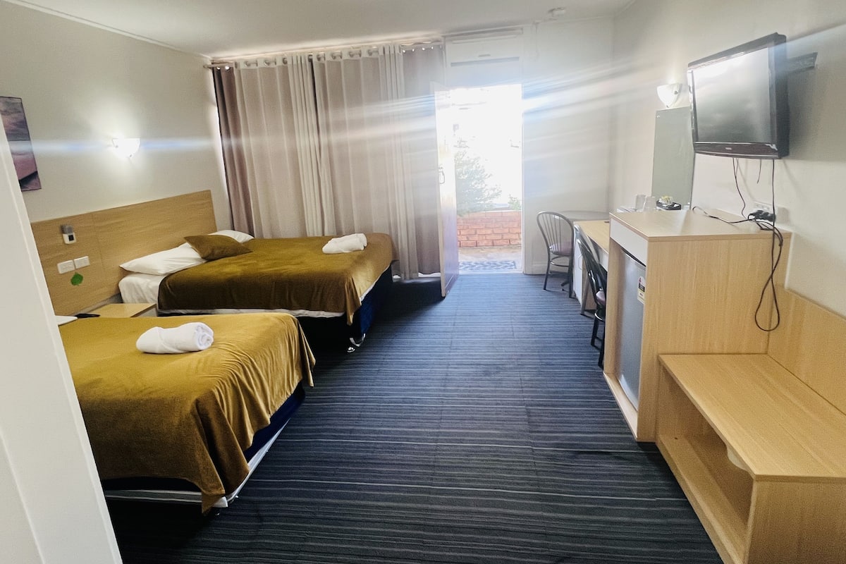A hotel room with two beds, a desk, a chair, a television, and a window with curtains.