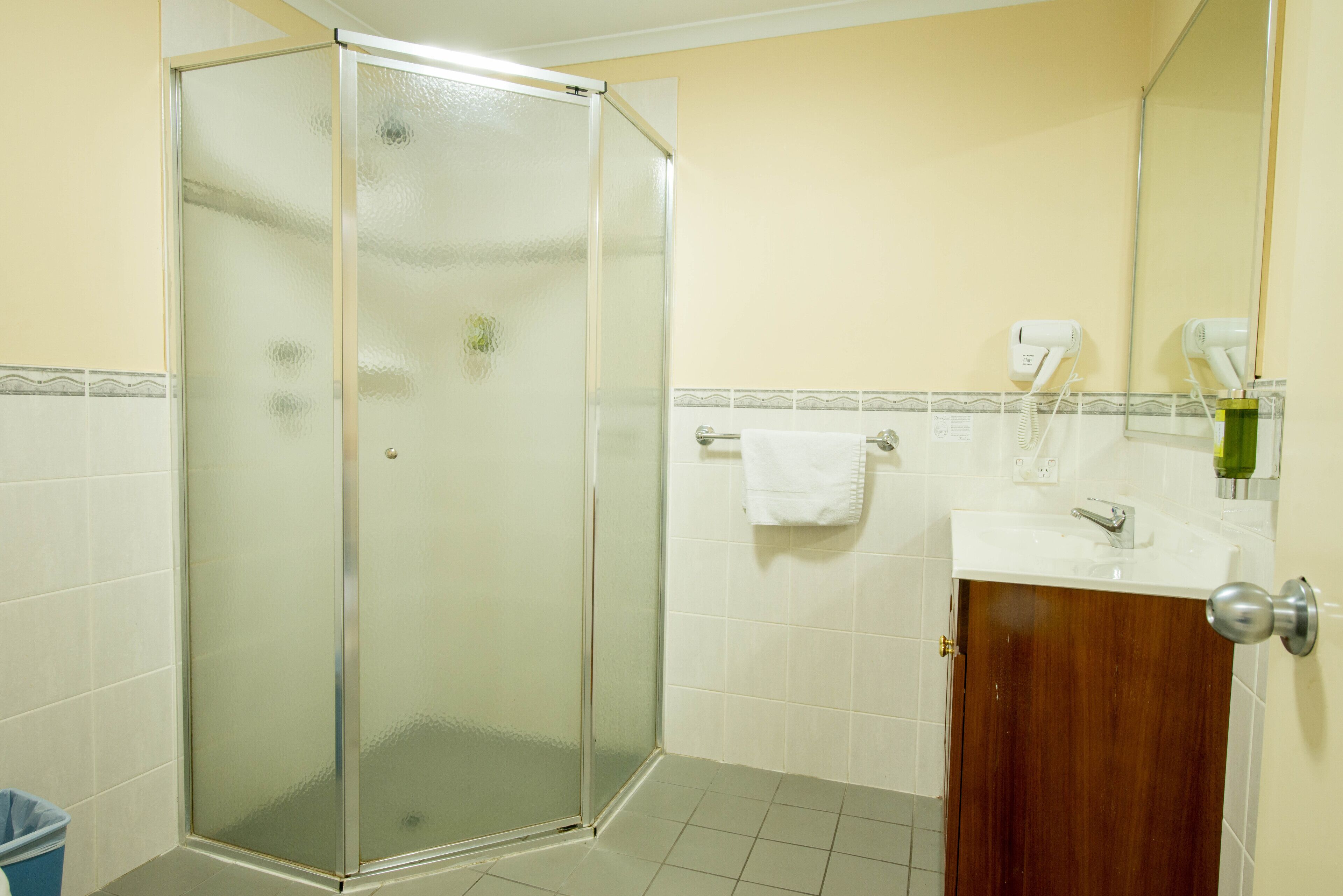 A bathroom with a glass-enclosed shower, a sink with a mirror, and a towel hanging on the wall.