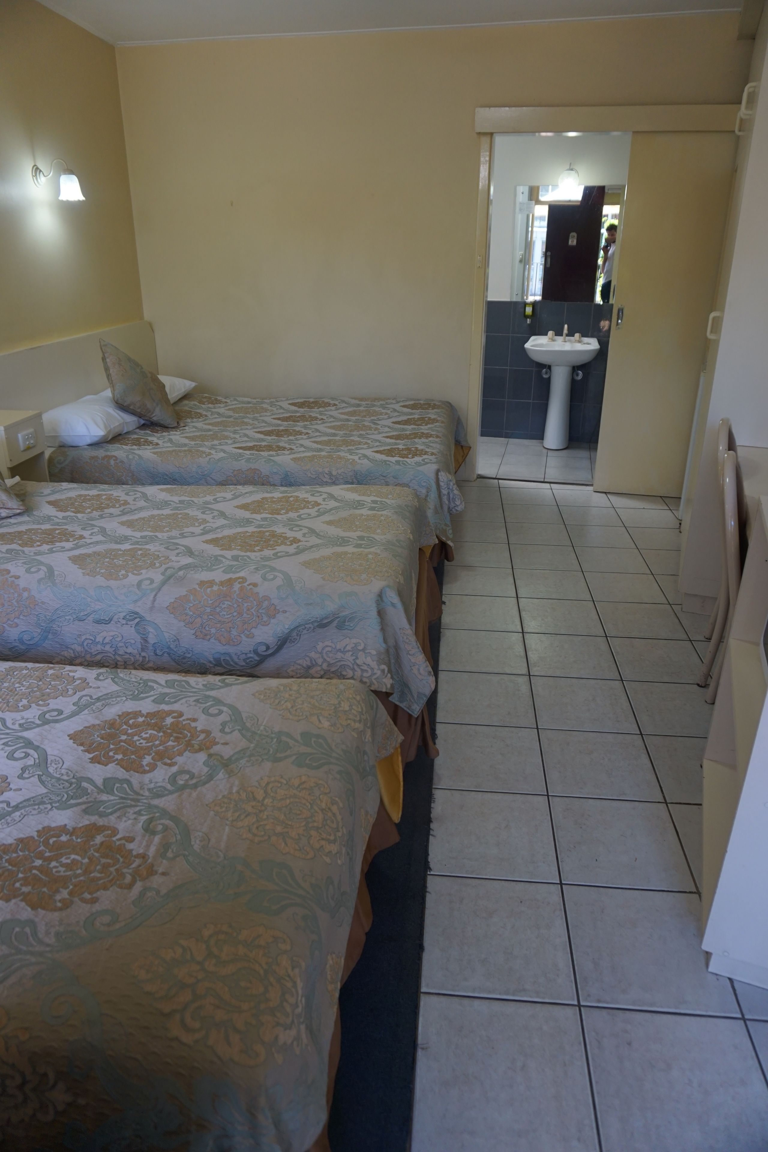 A hotel room with three beds, a bathroom with a sink, and a mirror.