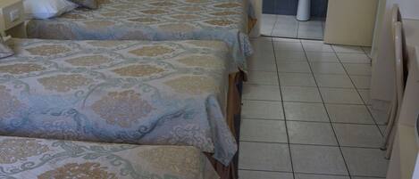 Habitación de hotel con tres camas, un baño con lavamanos y un espejo.