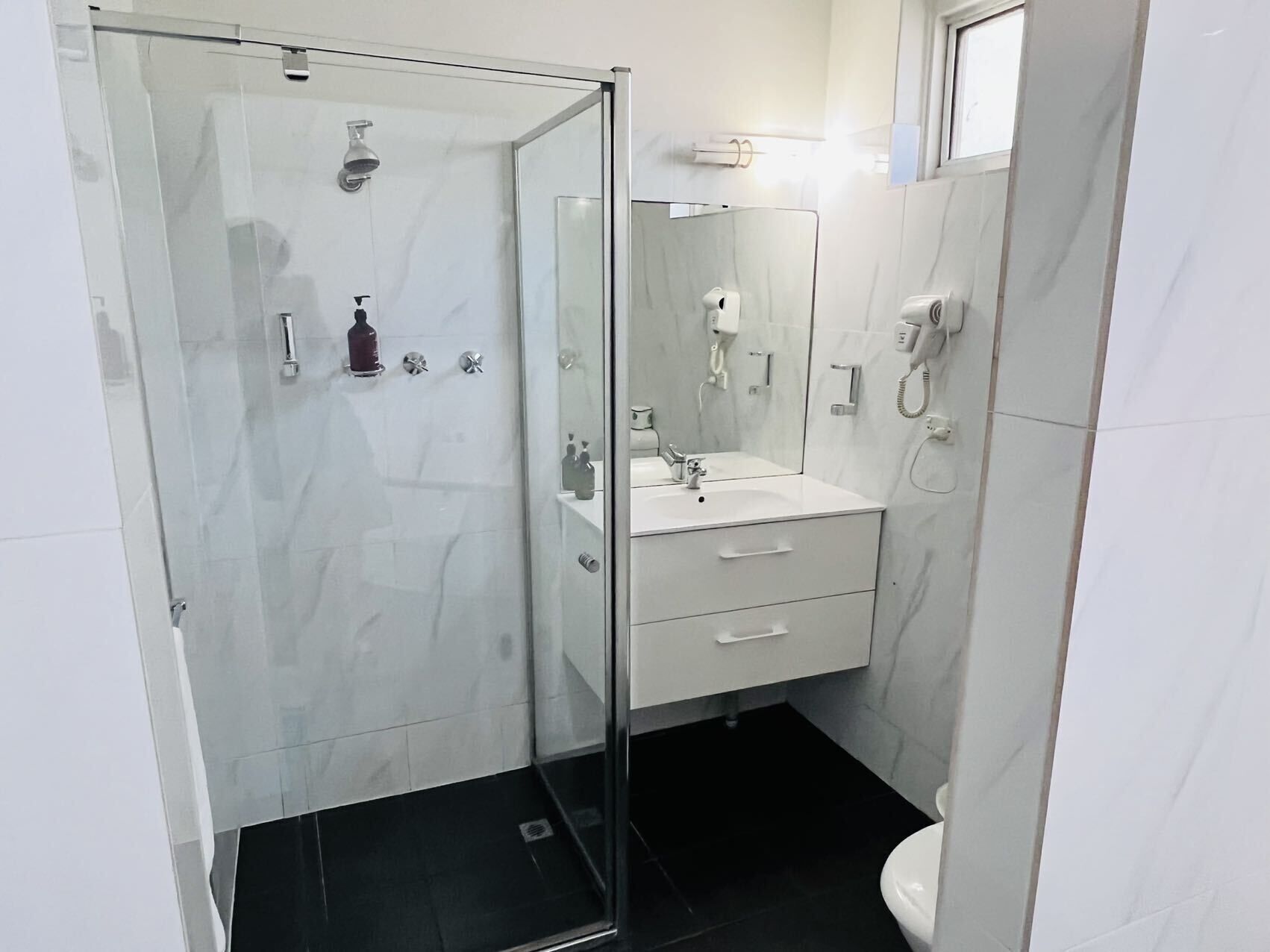Et moderne badeværelse med en brusekabine i glas, en hvid vask med spejl og et toilet.