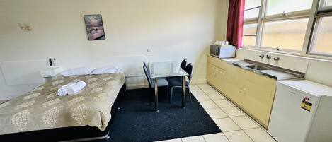Habitación de hotel compacta con cama, escritorio pequeño, kitchenette y ventana con cortinas.