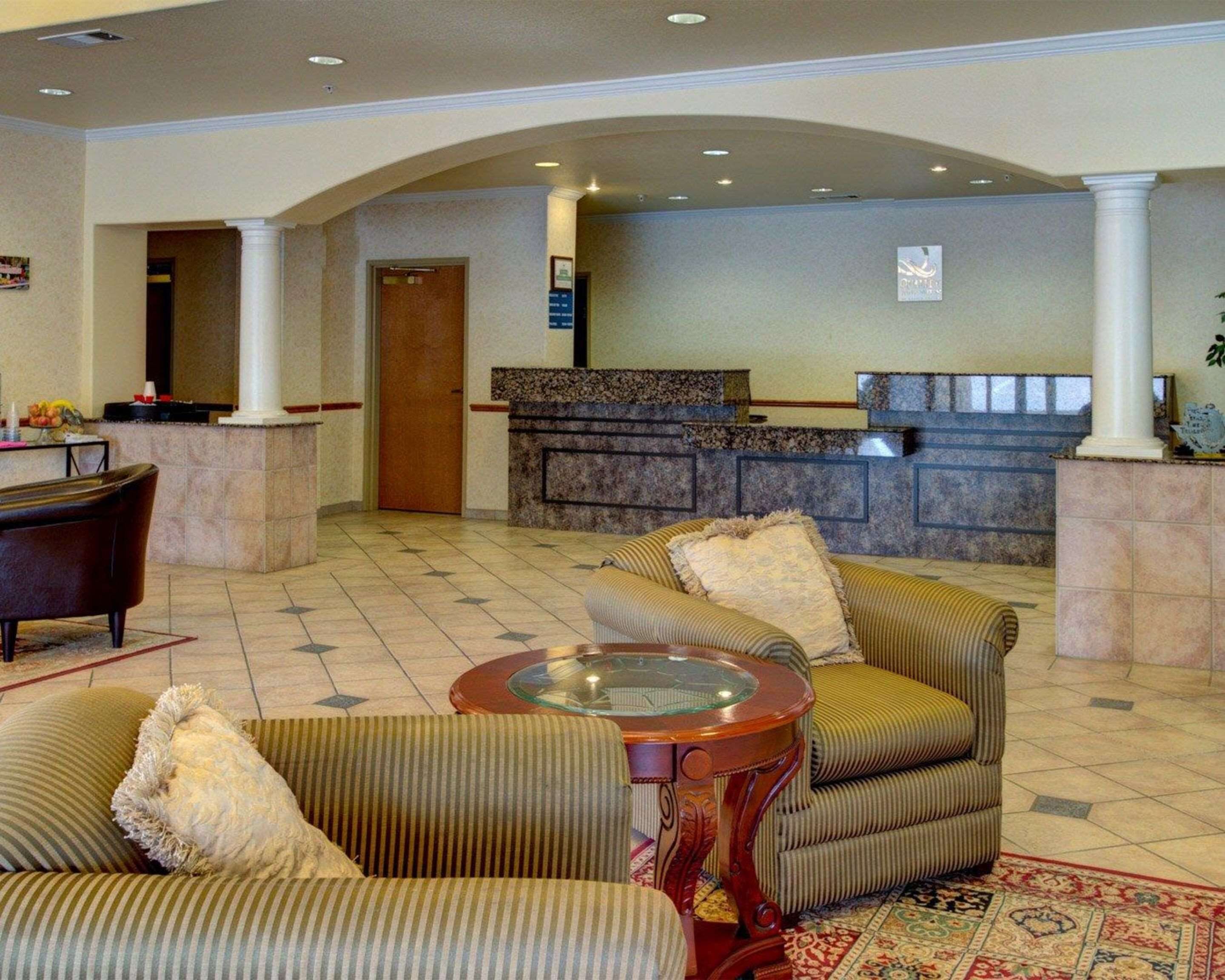 Un hall d'entrée avec des canapés à rayures, une table basse en verre, un comptoir d'accueil et un tapis à motifs.
