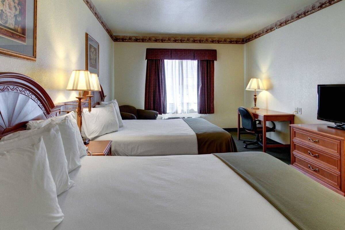 A hotel room with two beds, a desk, a television, and a chair.