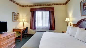 Una habitación de hotel con cama, escritorio, silla, televisor y dos lámparas.