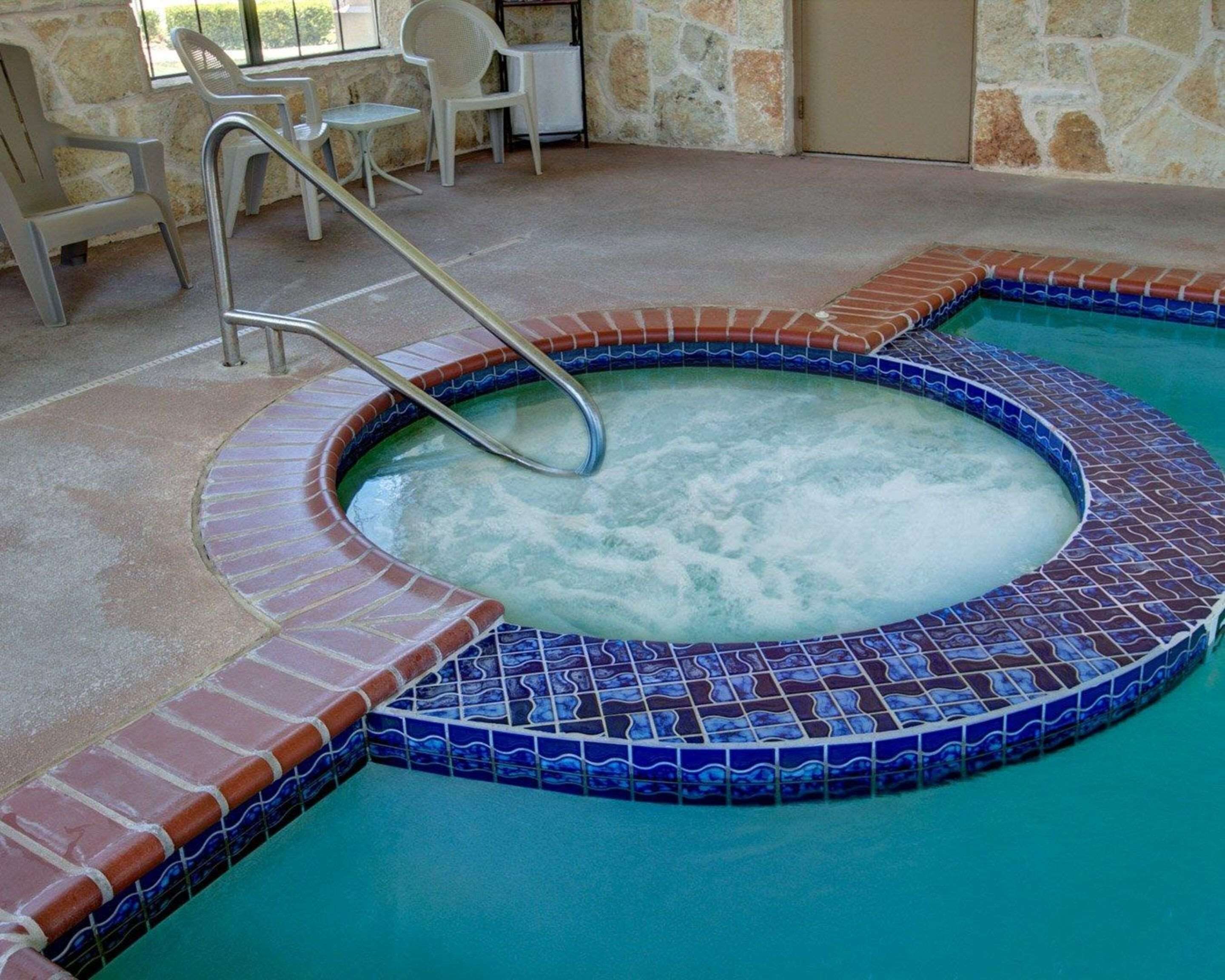 A hot tub with a tiled edge, surrounded by a stone wall and a tiled floor.
