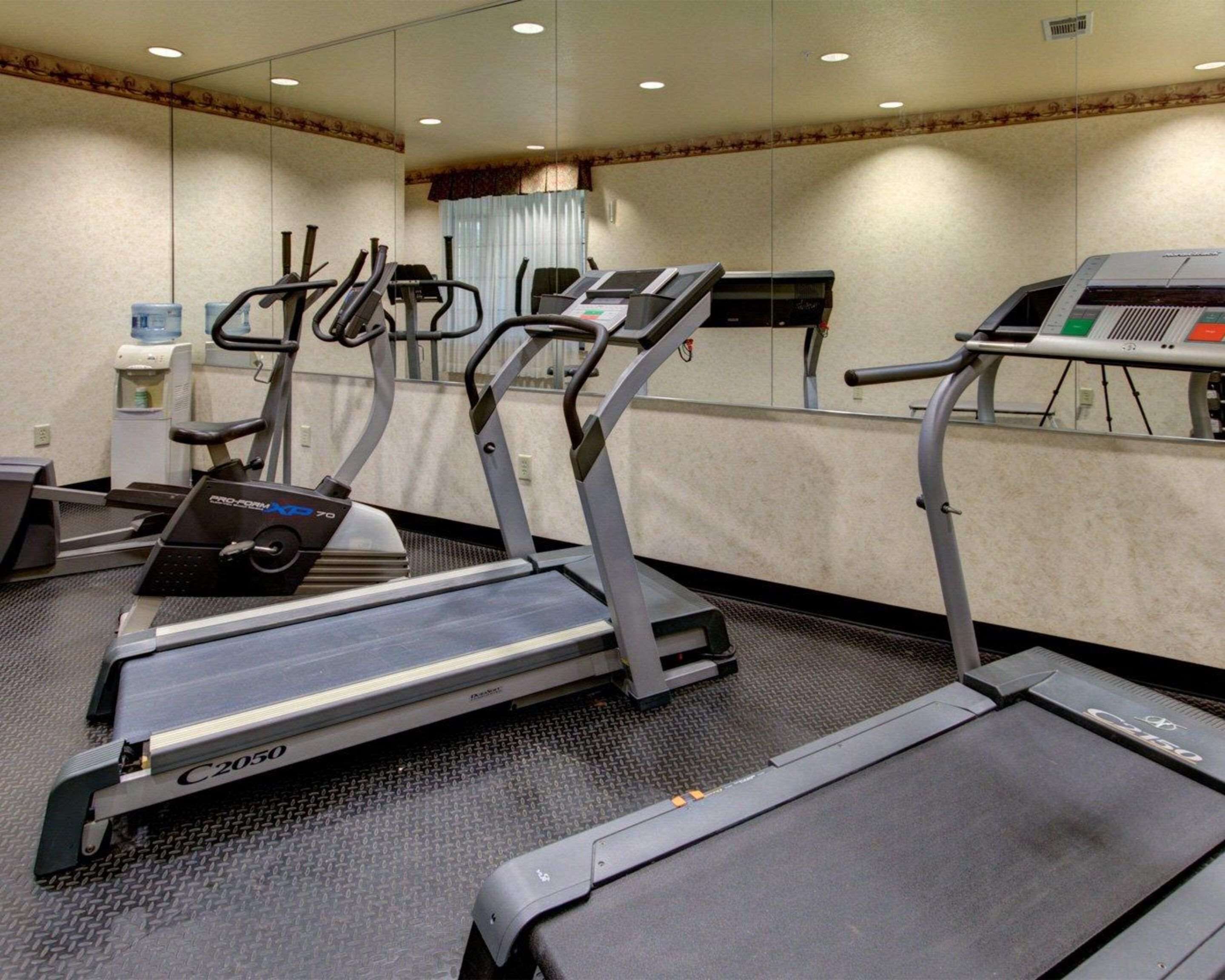 A fitness room with treadmills, a water dispenser, and a mirrored wall.