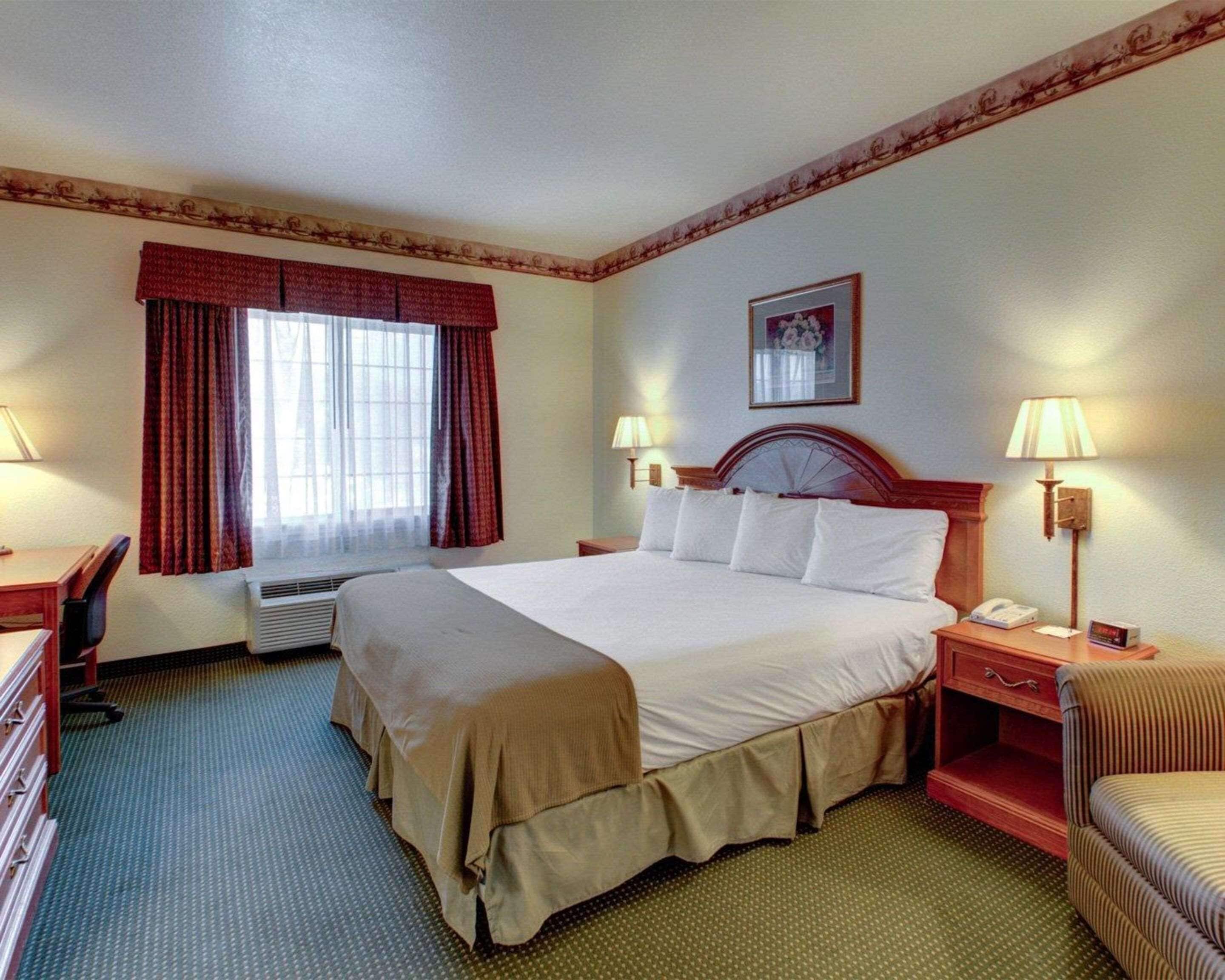 A hotel room with a large bed, two bedside tables with lamps, a desk, and a chair.