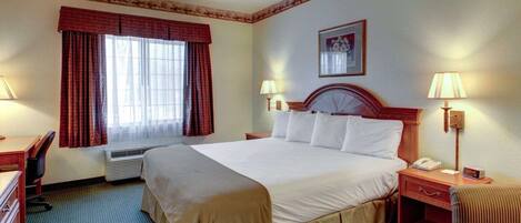 A hotel room with a large bed, two bedside tables with lamps, a desk, and a chair.