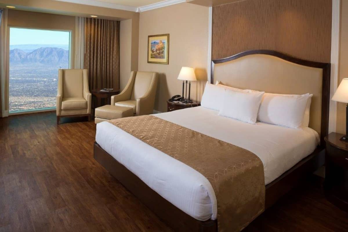 A hotel room with a large bed, two armchairs, a nightstand, and a view of the mountains.