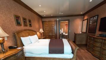 A hotel room with a bed, nightstands, a dresser, a TV, and a door leading to a bathroom.