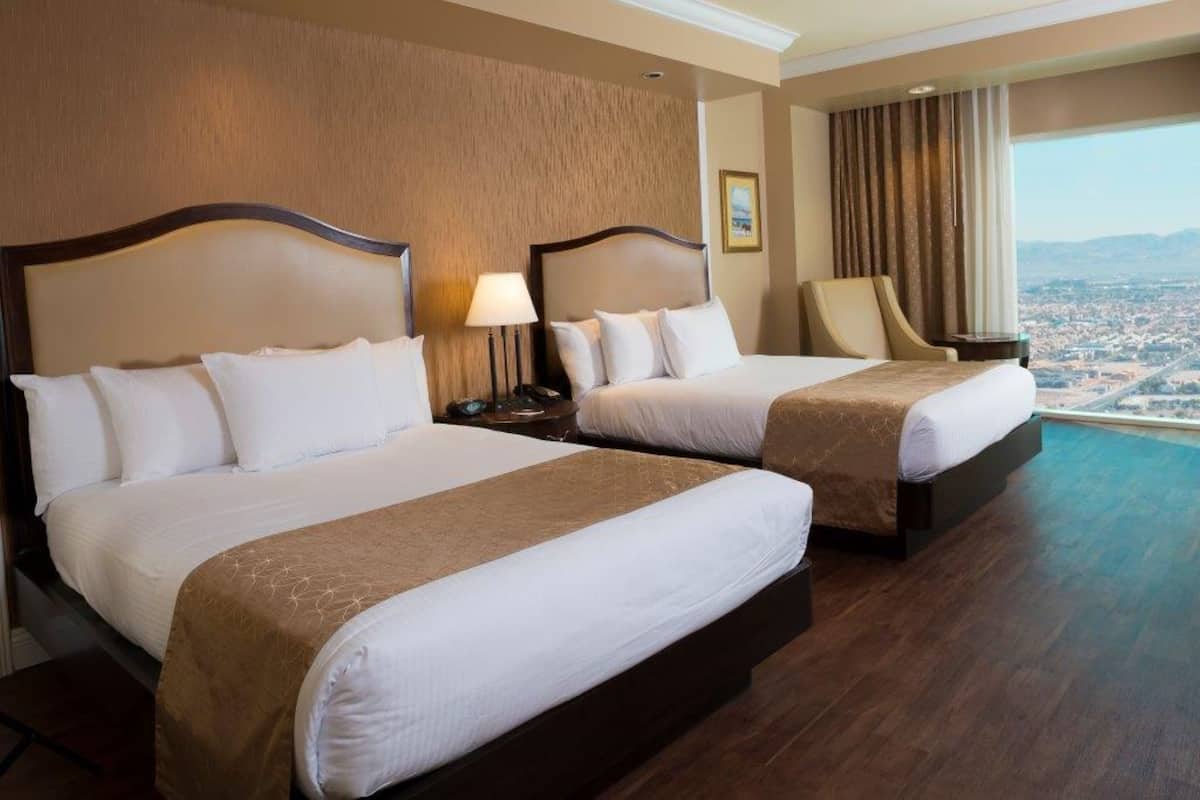 A hotel room with two beds, a view of a cityscape, and a large window with curtains.