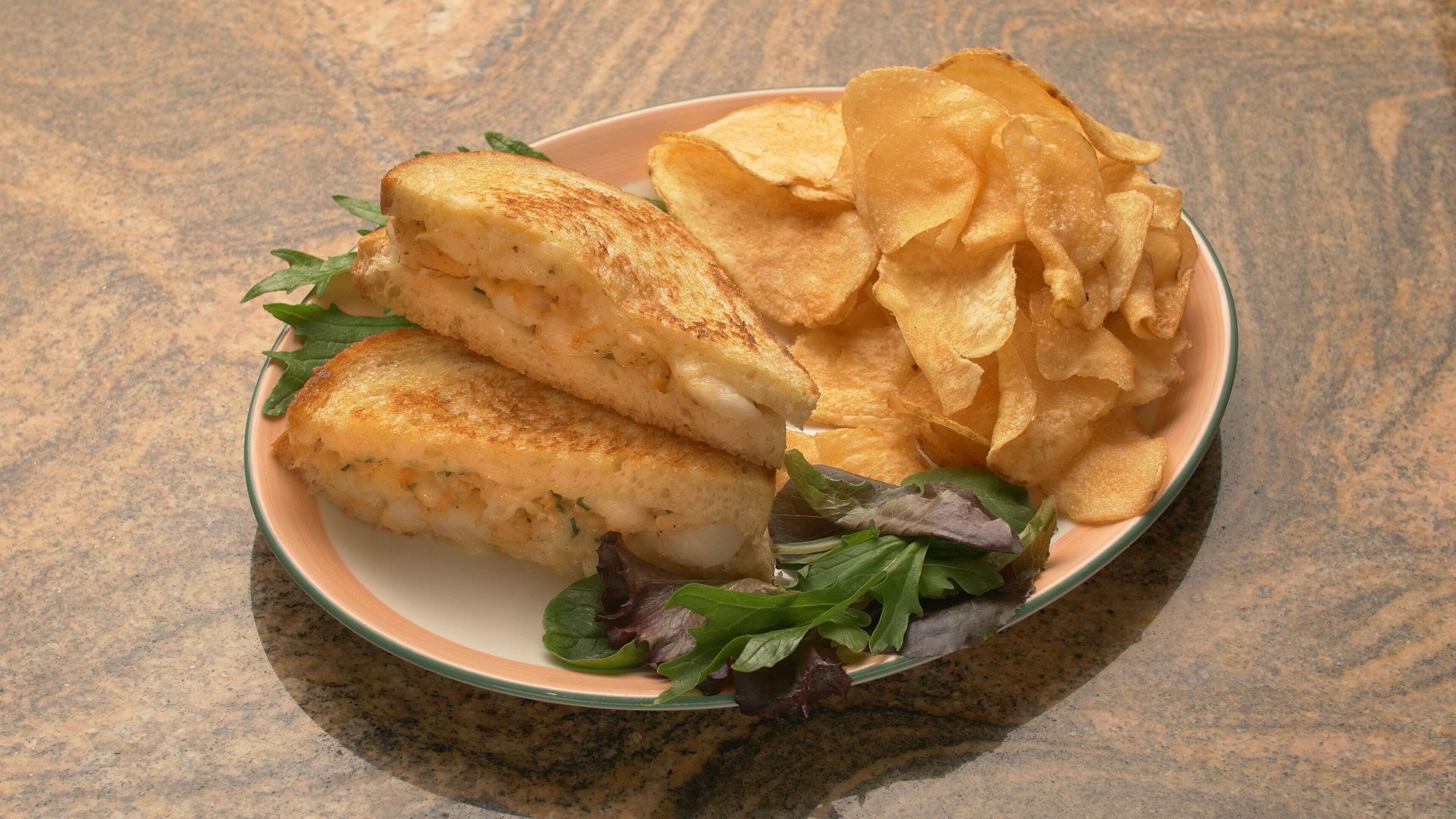 Une assiette avec des sandwichs au fromage grillé, des chips et une salade en accompagnement.