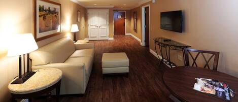 A hotel room with a sofa, ottoman, round table, and a TV mounted on the wall.
