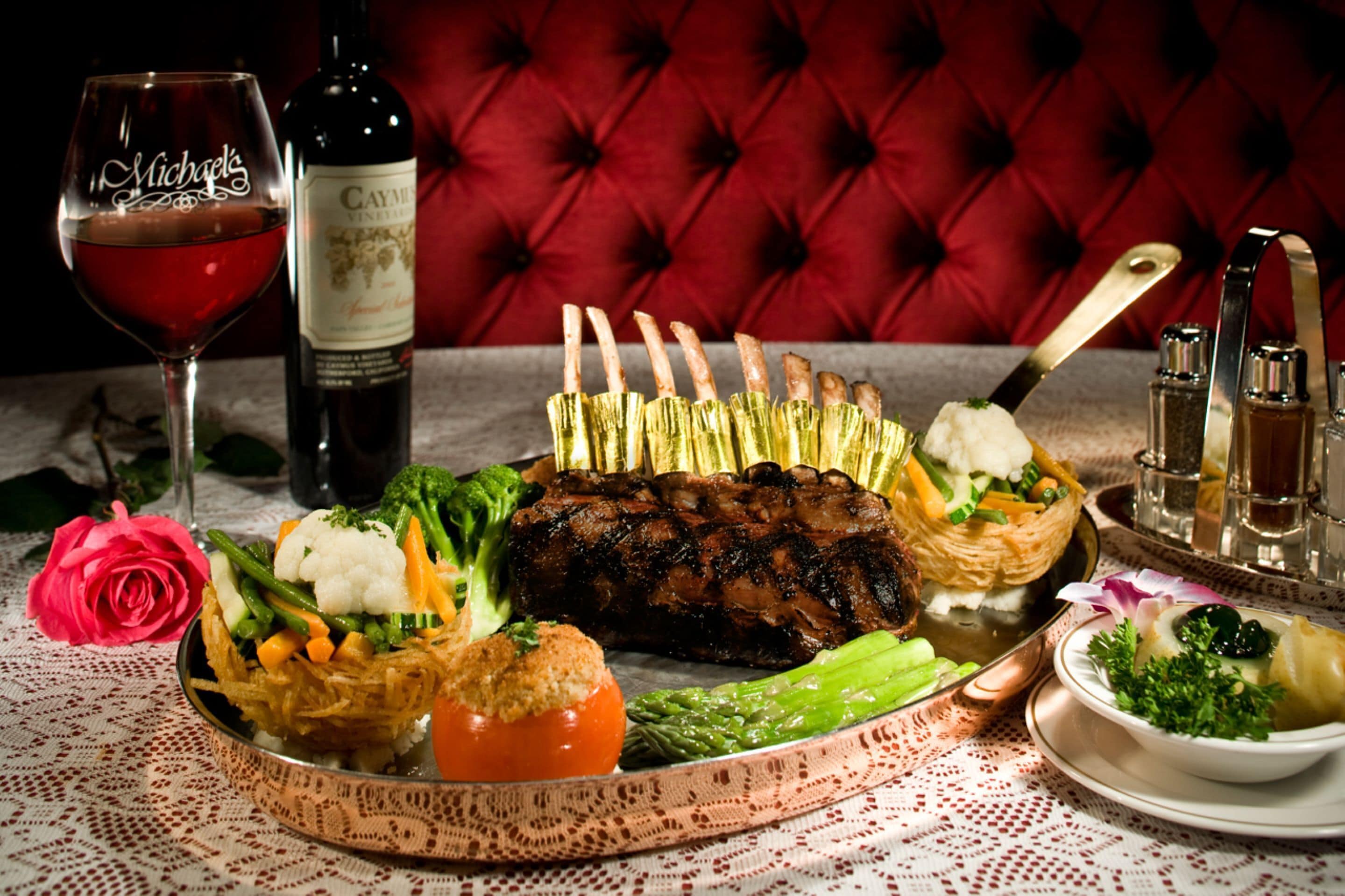 A dining table with a variety of dishes, including a roasted meat centerpiece, vegetables, and a rose. There are also wine bottles and glasses on the table.