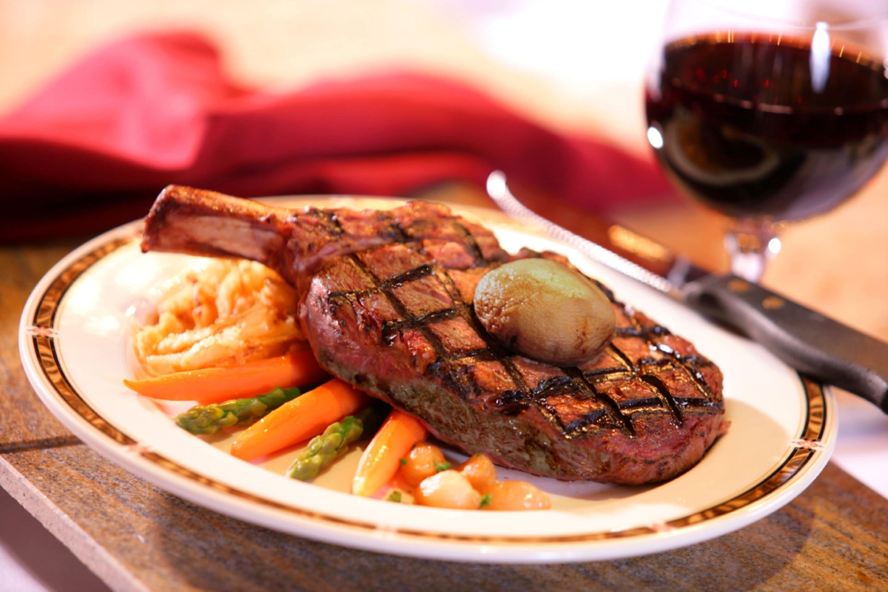 A plate with a grilled steak, asparagus, and carrots, accompanied by a glass of red wine.