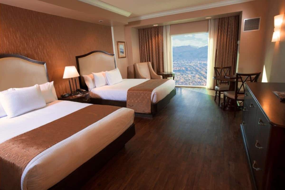 A hotel room with two beds, a desk, and a view of a cityscape.