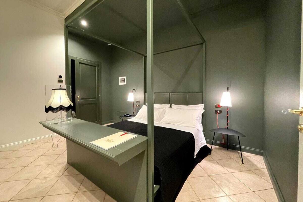 Una habitación de hotel con cama, mesita de noche, lámpara y espejo.