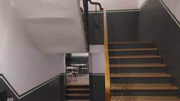 Una escalera de madera con barandas negras que conduce a una habitación con paredes blancas y suelo de baldosas.