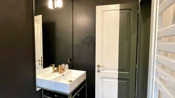 Une salle de bain avec un lavabo blanc, un miroir et une porte.