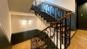 Una escalera con barandilla de madera y pasamanos de metal negro, que lleva a un piso superior.
