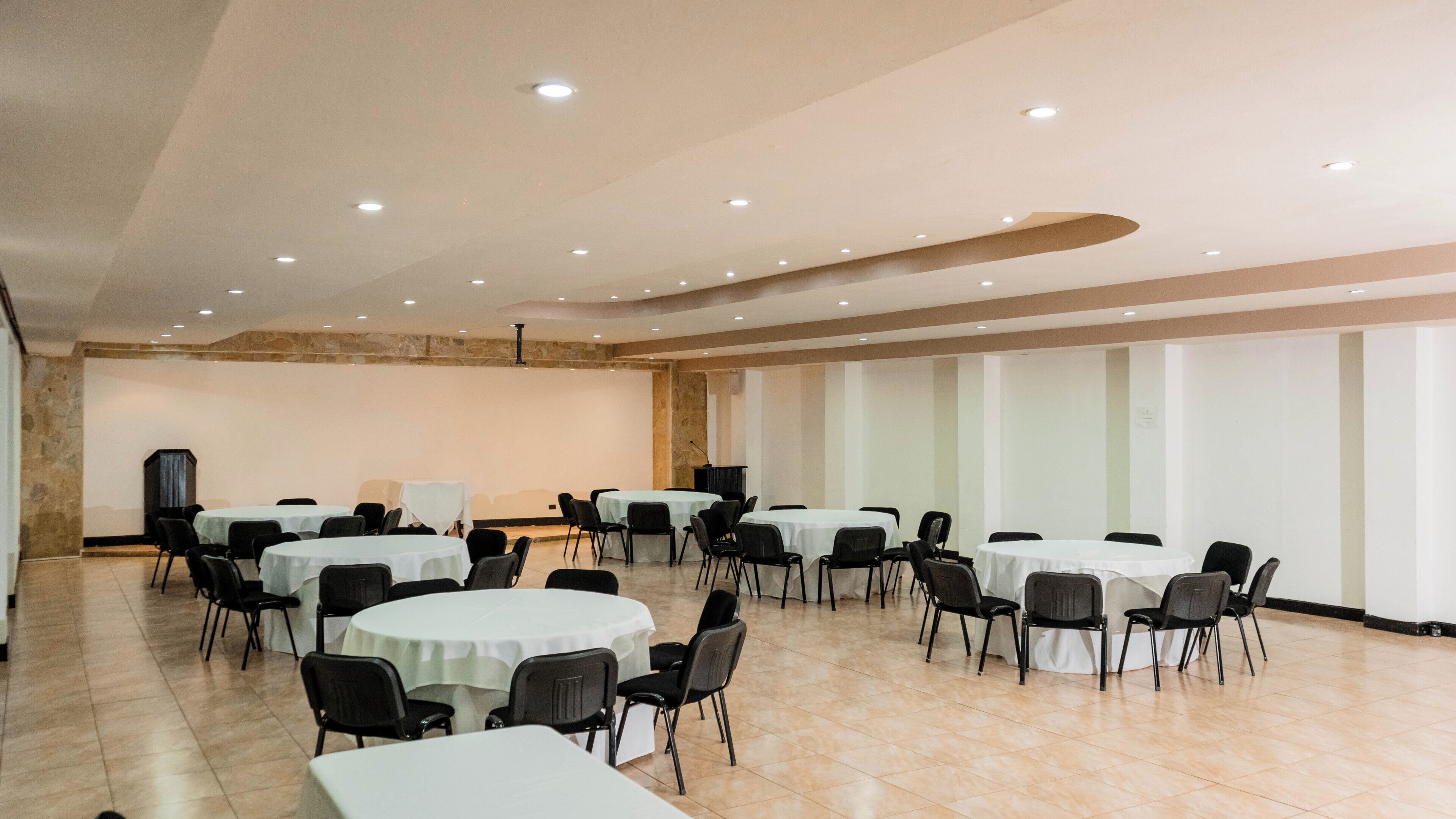 A conference room with multiple round tables and chairs, a stone accent wall, and a large whiteboard.