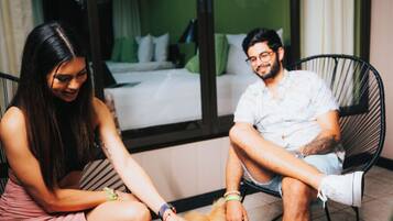 A couple seated on a balcony with a dog, overlooking a room with a bed and green walls.