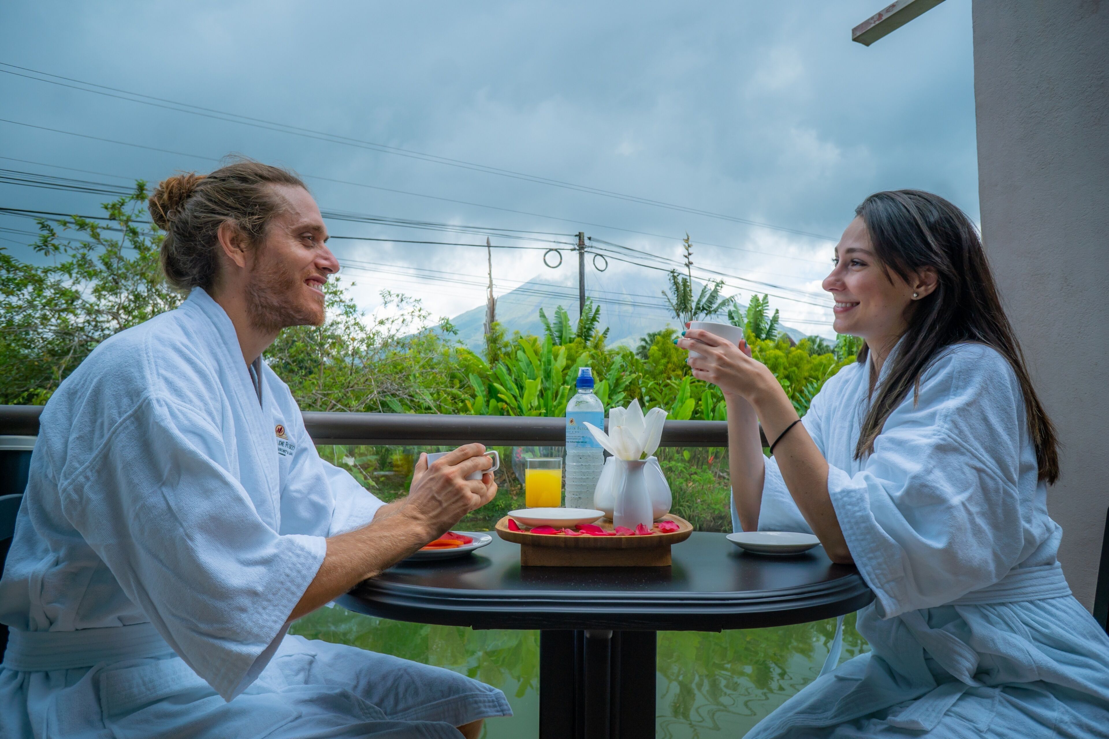 Two people sitting at a table with a meal, a glass of orange juice, and a bottle of water.