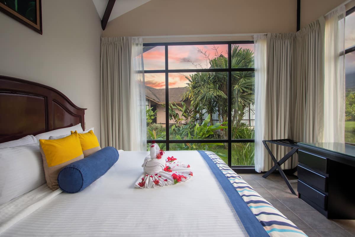 Une chambre d’hôtel avec un grand lit, un bureau et une vue sur la verdure par la fenêtre.