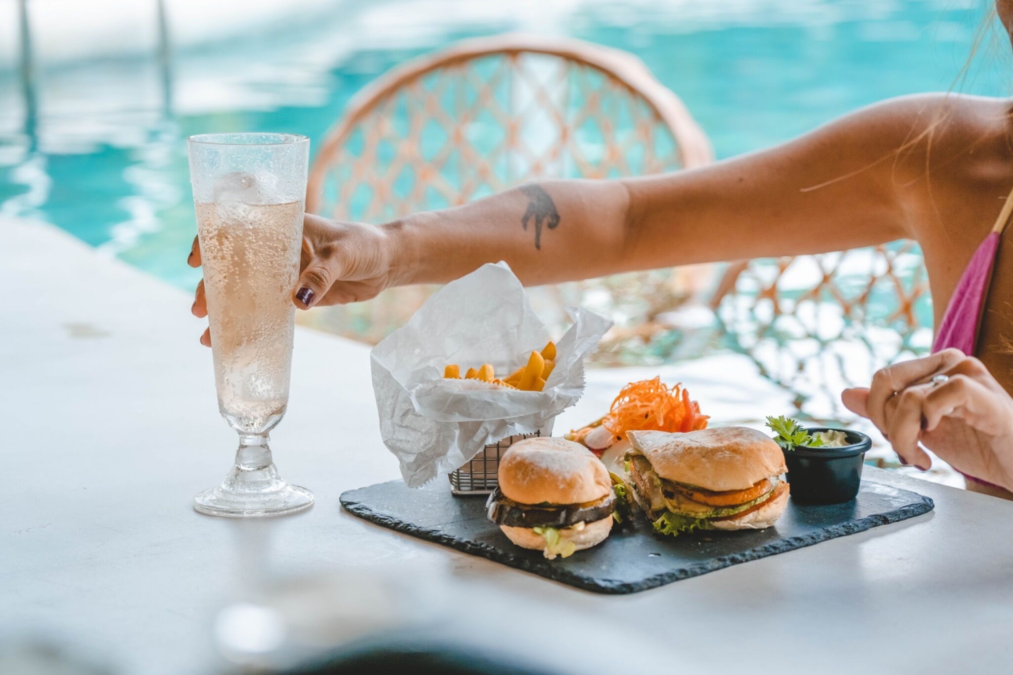 A dining table with a glass of iced beverage, two burgers, a side of fries, and a small salad.