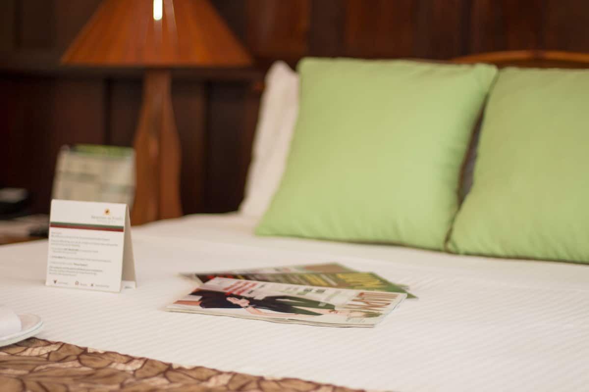 Un lit bien fait, avec des oreillers verts, une lampe et un magazine posés sur le lit.