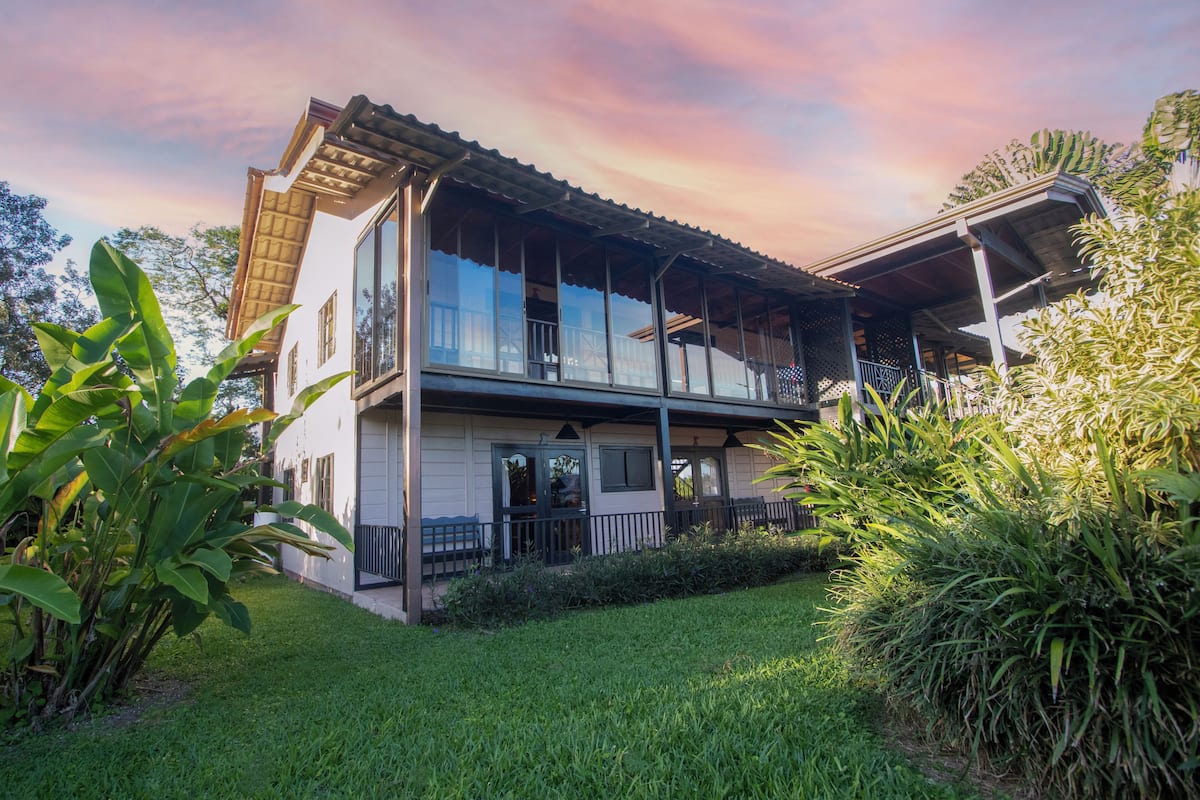 Une maison à deux étages dotée d’un balcon, entourée d’une végétation luxuriante.