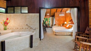 Une salle de bain avec une baignoire, une douche et des toilettes. On y trouve un lit avec des oreillers et une table de chevet avec une lampe.