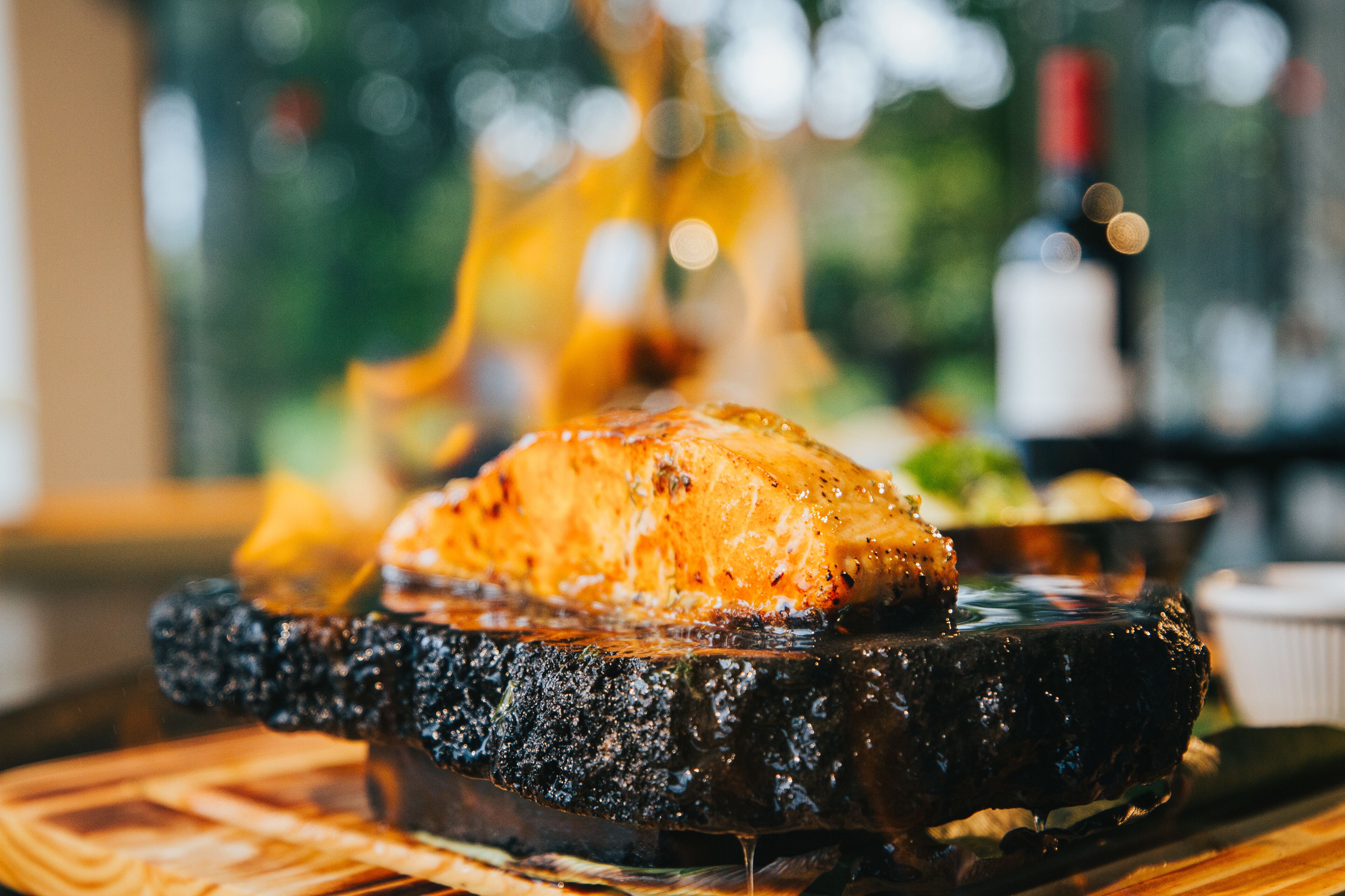 A grilled steak on a charred wooden board with a blurred background of a restaurant setting.