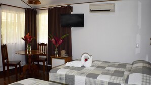 Hotelkamer met een bed, een aan de muur bevestigde televisie, een tafel met stoelen en een vaas met bloemen.