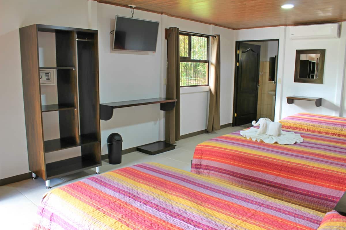 A hotel room with two beds, a TV, a window with curtains, a mirror, and a shelf.